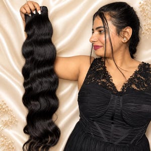 Puede incluir: Una extensión de cabello largo y ondulado en color negro profundo. El cabello presenta un patrón de ondas suave y constante en toda su longitud, con una apariencia densa y completa desde la trama superior hasta las puntas del cabello.