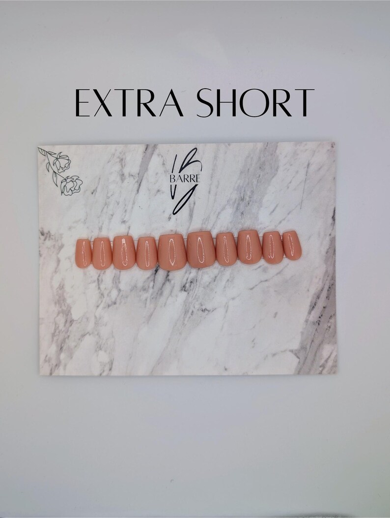 May include: A set of extra short, peach-colored press-on nails arranged on a marble-patterned surface. The nails are neatly aligned, showcasing a uniform shape and color. The text "EXTRA SHORT" is displayed above the nails, with the "Barre V" logo.