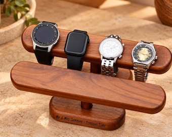 Op de afbeelding: Een houten horlogestandaard met twee niveaus en een gladde afwerking, met vier polshorloges op de bovenste balk. De voet is gegraveerd met de tekst "Mr & Mrs Jameson - Precious Time". De standaard heeft een horizontaal ontwerp met steun.