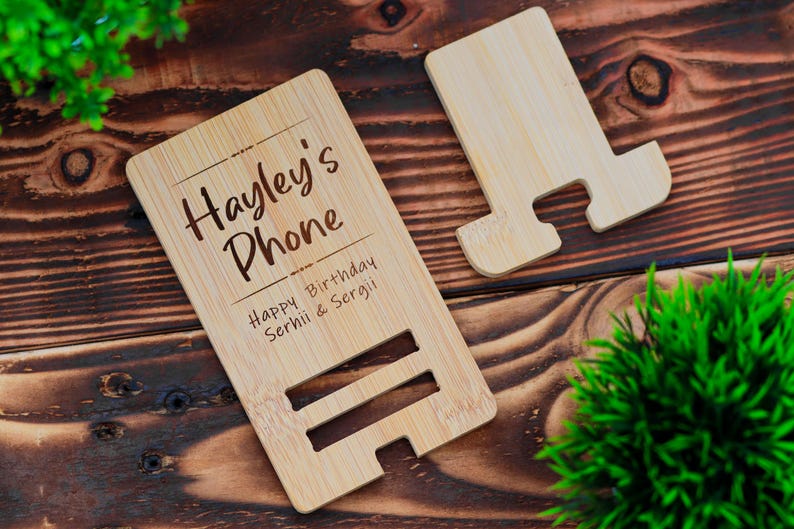May include: A personalized bamboo phone stand with the text "Hayley's Phone" and "Happy Birthday Serhii & Sergii" engraved on it.