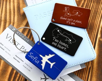 May include: Blue, black and brown luggage tags with white text and a map design. The blue tag says "Sofia" and has a white airplane silhouette. The black tag says "Two homes, one heart." The brown tag says "Home isn't a place, it's you."