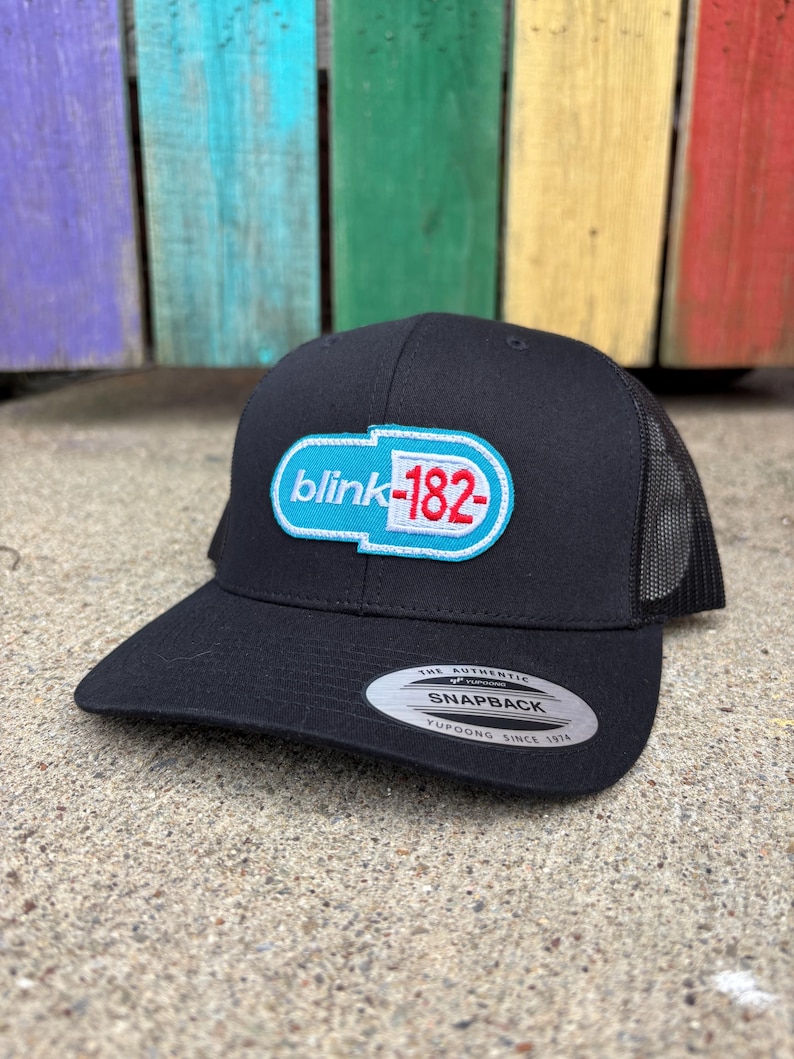 May include: Black snapback hat with a mesh back and a curved brim. The hat features a white, light blue, and red logo that says "blink-182". The hat has a snap closure and a Yupoong tag.