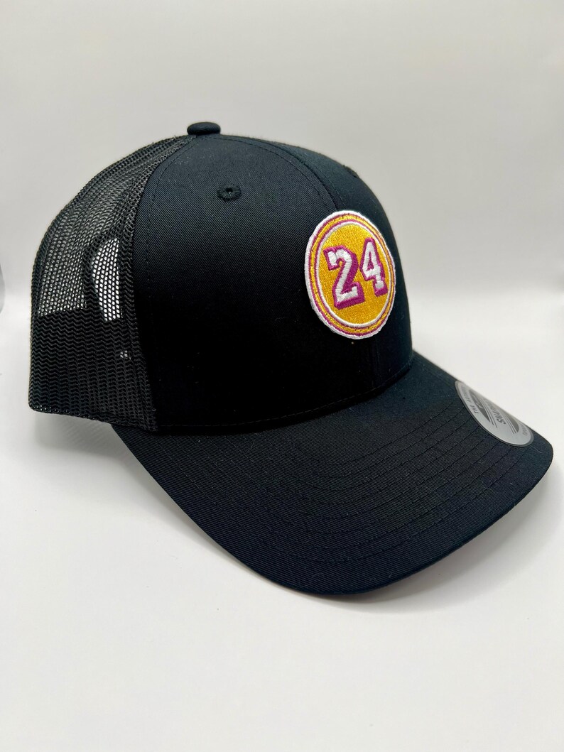 May include: Black trucker hat with a yellow and purple circle patch that says "24" on it.