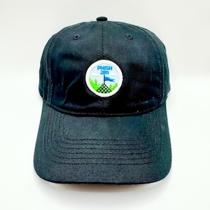May include: Black baseball cap with a curved peak. The cap has a circular patch with the text "PHISH 2011" in white, blue, and green. The patch shows a stylized landscape with a flag. The cap is made of a durable fabric.