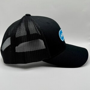 May include: Black trucker hat with a mesh back and a curved brim. The hat features a blue and white logo on the front panel. The hat has a snap closure for adjustable sizing.
