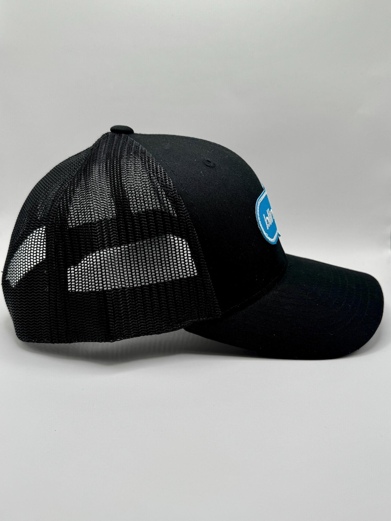 May include: Black trucker hat with a mesh back and a curved brim. The hat features a blue and white logo on the front panel. The hat has a snap closure for adjustable sizing.