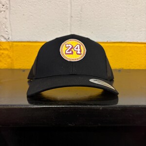 May include: Black trucker hat with a yellow and red circular patch that says "24" in white.
