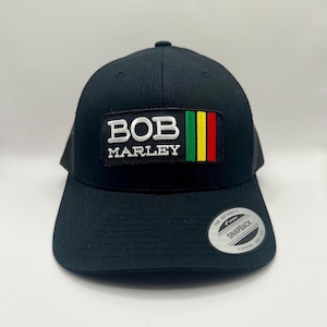 May include: Black trucker hat with a white "BOB MARLEY" patch and a red, yellow, and green stripe design. The hat has a black mesh back and a black adjustable snap closure.