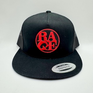 Op de afbeelding: Zwarte snapback pet met een rood geborduurd "RA QE" logo in een cirkel. De pet heeft een platte klep en een mesh achterkant. Een witte en zilveren sticker staat op de klep. Het is een Yupoong Snapback pet.