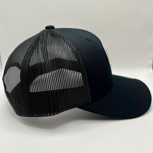May include: A black mesh trucker hat with a black brim. The hat has a black mesh back and a solid black front.