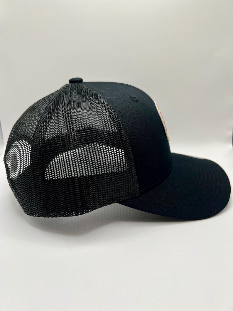May include: A black mesh trucker hat with a black brim. The hat has a black mesh back and a solid black front.