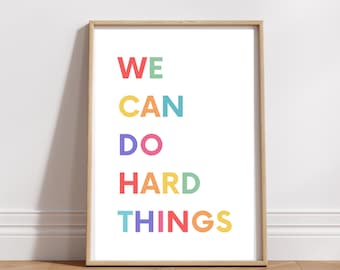 May include: A framed print with the text "WE CAN DO HARD THINGS" in rainbow colors. The words are stacked vertically, with each word in a different color.