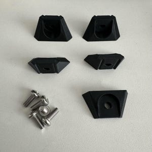 May include: Five black plastic corner brackets and five silver screws. The brackets have a triangular shape with a hole in the center.