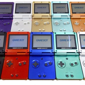 May include: A collection of ten Game Boy Advance SP handheld gaming consoles in various colors, including black, red, blue, green, silver, gold, and purple. Each console features the text "GAME BOY" on the screen.