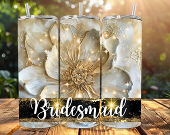 May include: Three stainless steel tumblers with a white and gold floral design and glitter accents. The tumblers have black lids and straws. The middle tumbler has the word "Bridemaid" in gold glitter lettering.