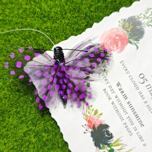 May include: A decorative butterfly with purple and black feathers and a black body. The butterfly has purple polka dots on its wings. The butterfly is on a white card with floral designs and the text "Every cloud has a silver lining".