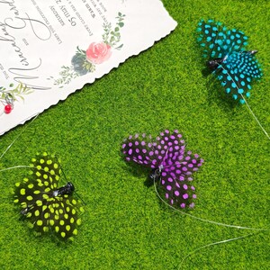 May include: Three decorative feather butterflies in teal, purple, and yellow with black polka dots, resting on a green surface. A wedding invitation with floral accents is in the background.