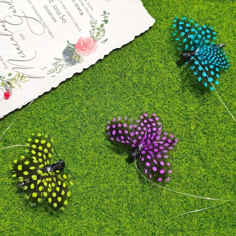 May include: Three decorative feather butterflies in teal, purple, and yellow with black polka dots, resting on a green surface. A wedding invitation with floral accents is in the background.