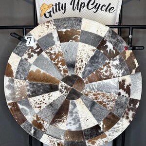 May include: A round dartboard made from cowhide patches in shades of brown, gray, and white. The dartboard has a circular design with a central bullseye and is mounted on a black metal stand. The text "Gitty UpCycle" is visible.