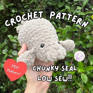 May include: A beige, chunky crochet seal plushie with black eyes. The image includes text that reads: CROCHET PATTERN, PDF Pattern!, CHUNKY SEAL LOW SEW!!. The plushie has a textured, soft appearance and is held against a background of green leaves.