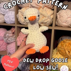 Puede incluir: Un patrón de crochet de un ganso blanco con pies y pico naranjas. La imagen incluye el texto "CROCHET PATTERN" y "DEW DROP GOOSE LOW SEW!". También es visible un corazón rojo con "PDF Pattern!". El ganso se muestra frente a estantes llenos de hilo.