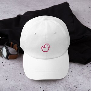 May include: White baseball cap with a pink pixelated duck embroidered on the front.