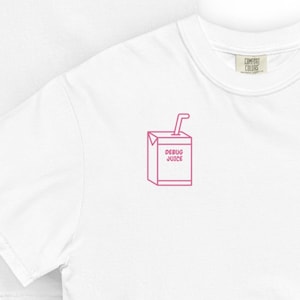 May include: White t-shirt with a pink graphic of a juice box that reads "DEBUG JUICE". The shirt is made by Comfort Colors. The juice box has a straw and is outlined in pink.