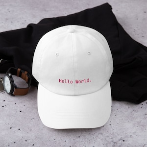 Könnte beinhalten: Weiße Baseballkappe mit einem rosa gestickten "Hello World." Text.