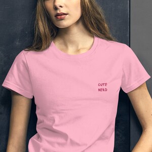 Op de afbeelding: Een roze T-shirt met de tekst "Cute Nerd" in roze letters.