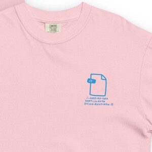 Op de afbeelding: Lichtroze T-shirt met een blauwe afbeelding van een bestand en de tekst "i-HAVE-NO-IDEA WHAT-IM-EVEN DOING-RIGHT-NOW.JS". Het shirt heeft een ronde hals en het "COMFORT COLORS" logo.