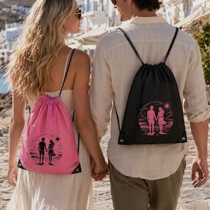 K&ouml;nnte beinhalten: Ein pinkfarbener und ein schwarzer Turnbeutel mit Kordelzug, beide mit einem Grafikdruck von zwei Personen, die sich am Strand unter einer Sonne an den H&auml;nden halten. Die Beutel haben schwarze Kordeltr&auml;ger und verst&auml;rkte &Ouml;sen an den Ecken.