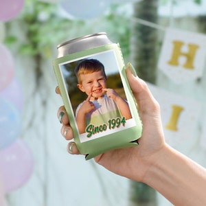 May include: Green can cooler with a photo of a young boy smiling and pointing to his teeth. The text "Since 1994" is printed on the cooler.