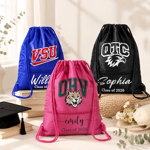 May include: Three drawstring backpacks in blue, pink, and black. The blue bag has "VSU" in red and white, the pink bag has "OHV" and a wildcat graphic, and the black bag has "OTC" and an eagle graphic. Each bag has a name and "Class of 2026".