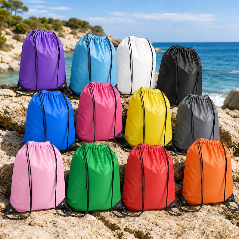 May include: A collection of twelve drawstring bags in various solid colors including purple, light blue, white, black, blue, pink, yellow, gray, light pink, green, red, and orange, each featuring black cord straps and a cinched top closure.
