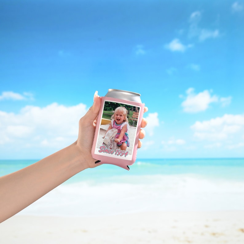 May include: Pink can cooler with a photo of a young girl on a swing set. The text "Since 1994" is printed on the cooler.