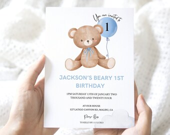 May include: A light blue and white birthday invitation card featuring a watercolor illustration of a teddy bear holding a blue balloon with the number 1. The text reads "Jackson's Beary 1st Birthday".