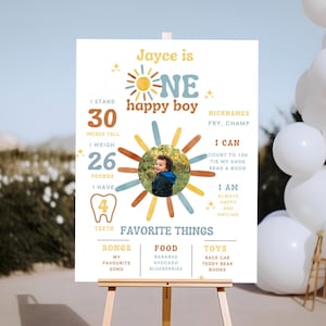 Può includere: Un cartello di compleanno personalizzato su un cavalletto. Mostra una foto di un bambino, misure di 76 cm di altezza e 11,8 kg, e il testo "Jayce is ONE happy boy". Sono elencate le cose preferite.