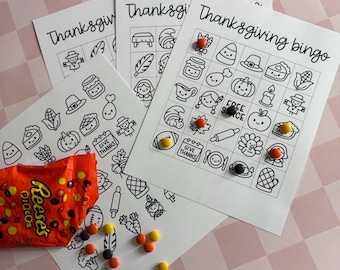 May include: Thanksgiving bingo game sheets with illustrated icons and the words "Thanksgiving Bingo". A bag of Reese's Pieces candies and colorful candies are scattered around the sheets. The background is a pink and white checkered pattern.