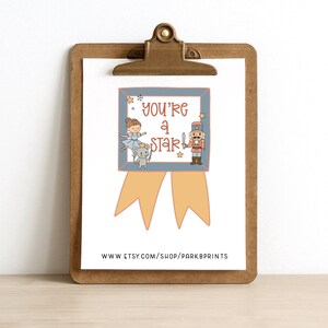 May include: A print on a clipboard with the text "You're a Star" and illustrations of a ballerina, a mouse, and a nutcracker. The print has a blue border and tan ribbon design. The clipboard is brown.