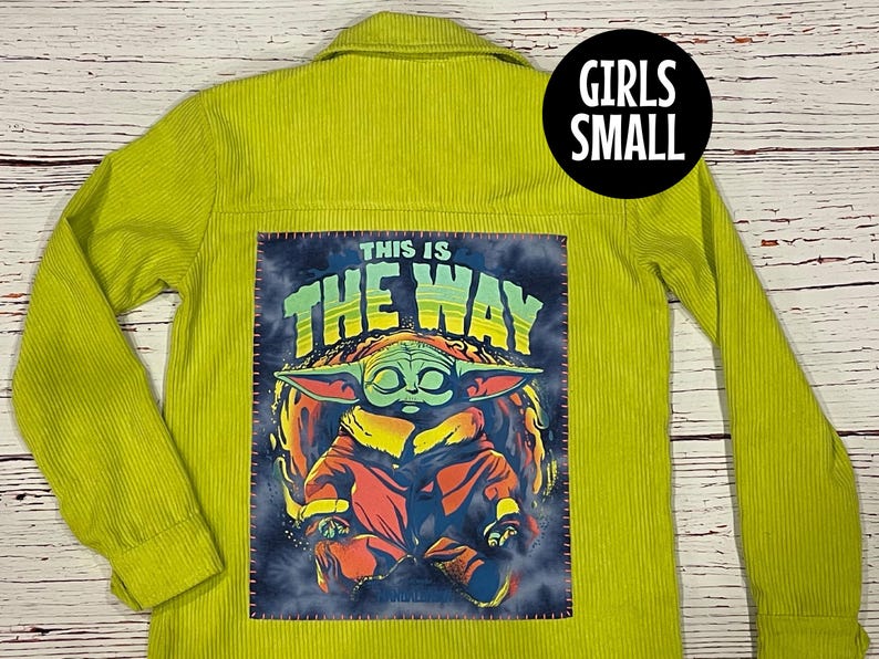 Op de afbeelding: Een limoengroen corduroy jack met een patch op de rug. De patch toont een cartoonfiguur met de tekst "This is the way".