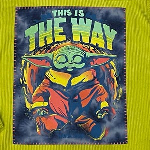 Op de afbeelding: Een geel corduroy shirt met een groene, gele en rode afbeelding van een personage uit de Star Wars-franchise, bekend als "Baby Yoda", met de tekst "This is the way".