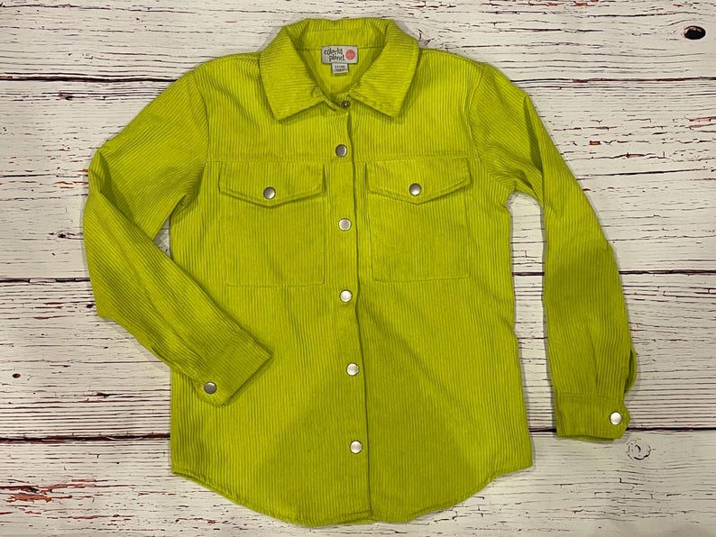 Op de afbeelding: Een limegroen corduroy overhemd met lange mouwen en twee borstzakken. Het shirt heeft een klein wit label met de tekst "Girls Like" erop.