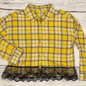 May include: Yellow and black plaid flannel shirt with a black lace trim. The shirt has long sleeves and a button-up front.