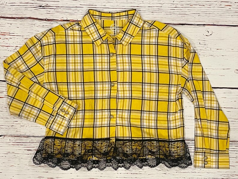 May include: Yellow and black plaid flannel shirt with a black lace trim. The shirt has long sleeves and a button-up front.