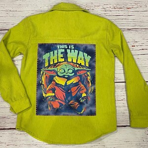 Op de afbeelding: Een limoengroen corduroy overhemd met een patch op de rug met een cartoonfiguur met de tekst "This is the way".