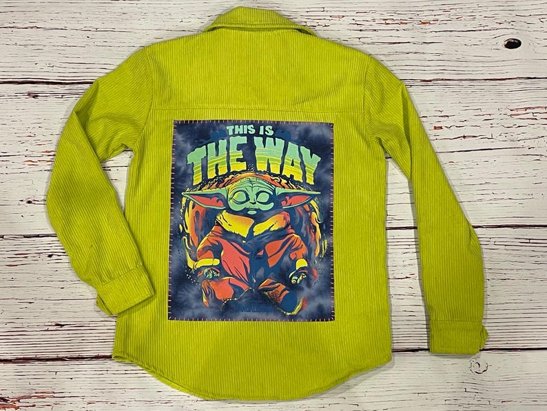 Op de afbeelding: Een limoengroen corduroy overhemd met een patch op de rug met een cartoonfiguur met de tekst "This is the way".