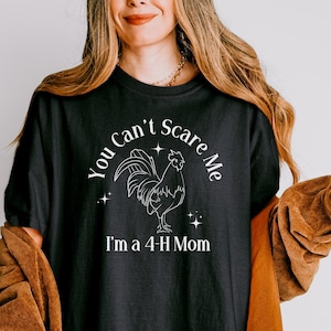 Peut inclure: Un t-shirt noir avec un graphique de coq blanc et le texte "You Can't Scare Me I'm a 4-H Mom".