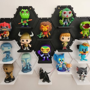 May include: A black and white hexagonal shelf unit with white shelves displays a variety of colorful pop culture figurines. The figurines include characters from Star Wars, He-Man, Scooby Doo, and Tom and Jerry.
