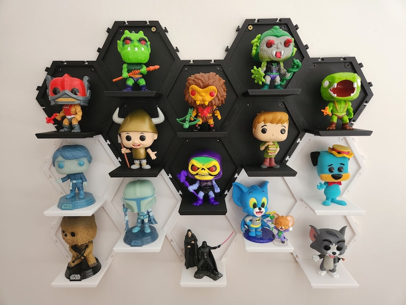 May include: A black and white hexagonal shelf unit with white shelves displays a variety of colorful pop culture figurines. The figurines include characters from Star Wars, He-Man, Scooby Doo, and Tom and Jerry.