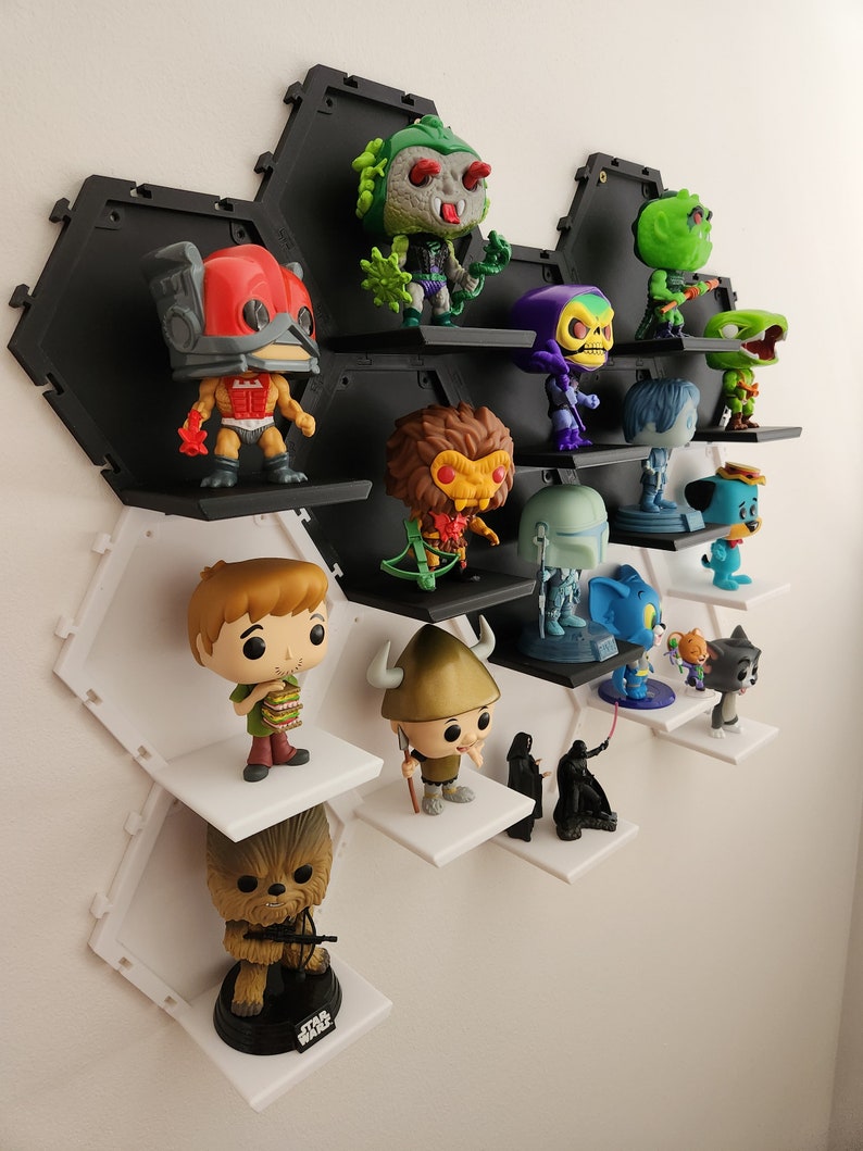 May include: A hexagonal shelf unit with white and black shelves displays a collection of pop culture figurines. The figurines include characters from Star Wars, Scooby Doo, and other popular franchises.